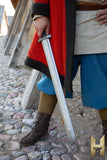 Person in historical or fantasy attire holding a sword on a stone path.