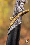 Close-up of a dagger with detailed handle design against a blurred natural background