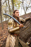 Person in fantasy costume with sword leaning against a tree in a forest setting