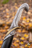 Decorative dagger handle with intricate designs against a blurred natural background
