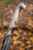 Decorative sword hilt with intricate designs against a blurred natural background