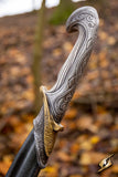 Decorative sword handle with intricate patterns against a blurred natural background
