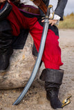 Person in pirate costume holding a sword on a log outdoors
