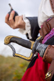 Close-up of a sword with a detailed hilt held by a person in historical attire.