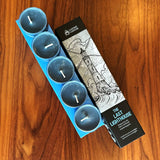 Set of blue candles in a box with a packaging featuring 'The Last Lighthouse' design on a wooden surface.