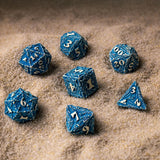 Set of blue polyhedral dice with metallic sheen on a sandy surface