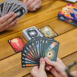 Person holding a deck of tarot cards on a wooden table with other cards spread out.