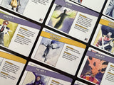 A close-up, angled view of several illustrated trading cards arranged in a grid. The cards feature fantasy artwork and text boxes with purple, yellow, and white design elements.