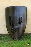 Black shield with straps on a grassy ground against a beige wall