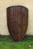 Wooden shield with a black rim on a grassy ground against a beige wall.