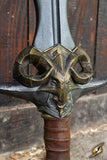 Close-up of a sword with ornate ram's head hilt against a wooden background