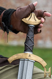 Hand holding a sword with a detailed hilt against a blurred natural background