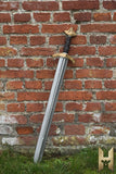 Sword with a gold hilt leaning against a brick wall.