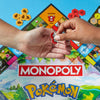 Two hands holding a Pokémon-themed Monopoly piece against a colorful Monopoly board game background.