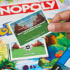 Hand holding a Pokémon-themed card over a Monopoly board game