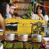 Table with 'Homestead' product packaging and candles, people in the background