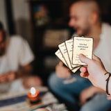 Person holding cards with blurred people and candle in the background