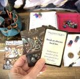 Hand holding a game card with text and illustration, surrounded by other game components on a table.
