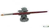 Paintbrush held by a small dragon-like figurine on a white background