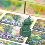 Green dragon figurine on a board game with colorful cards featuring dragons and hearts.