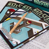 Close-up of 'MAZESCAPE' game cards with a wooden stick on top