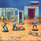 Toy figures on a miniature battlefield with 'Masters of the Universe Battleground' branding.