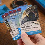 Hand holding game cards with an eagle illustration and 'Good Eyesight' text on a wooden surface.
