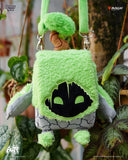 Green plush bag with a black face design on a plant background