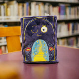 Plush toy with a design of a path leading to a star, placed on a table in a library setting.