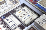Close-up of a card game with various cards and pieces on a light surface.