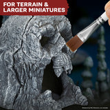 Hand holding a brush over a textured miniature rock with text 'FOR TERRAIN & LARGER MINIATURES' at the top.