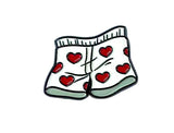 Pin with cartoon shorts featuring red hearts on a white background