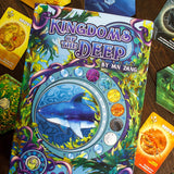 Card game packaging titled 'Kingdoms of the Deep' by HN Zang on a wooden surface with other cards.