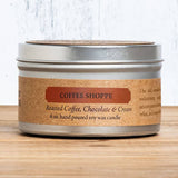 Candle in a metal tin labeled 'Coffee Shoppe' on a wooden surface.