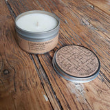 Candle in a tin with a decorative lid on a wooden surface