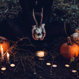 Person holding a skull with antlers over candles and pumpkins in a dark setting
