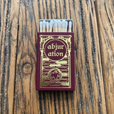 Matchbox with 'abjur ation' design on a wooden surface