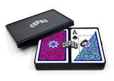 A black playing card deck box shown open on a white background, with the lid leaning behind the deck. The deck contains cards with red and blue ornamental backs, and the top card is an Ace of Spades with a black and blue shield design.