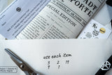 Newspaper with 'Special Edition' text, scissors, and a piece of paper with numbers on a white surface.