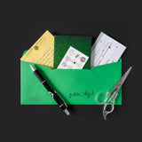 Green envelope with stationery items including a pen, scissors, and cards on a black background.