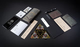 Collection of stationery items including notebooks, cards, and a pen on a dark surface.