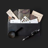 Collection of stationery items including cards, a pen, and a small round object on a black background.
