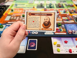 Hand holding a game card over a board game with colorful tiles