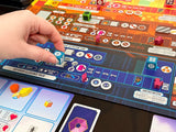 Board game in progress with a hand rolling a die