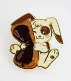 Enamel pin of a rabbit holding a book on a white background