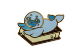 Blue cartoon seal pin with gold accents on a white background