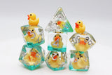 A set of clear acrylic polyhedral dice with yellow rubber ducks embedded inside, featuring silver-colored numbering. The set includes a D4, D6, D8, D10, D12, D20, and D24, arranged on a white background.