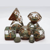 A set of transparent polyhedral gaming dice with embedded green and brown forest-themed illustrations, featuring metallic bronze numbers and two small skull-shaped d6 dice, arranged on a light gray background.