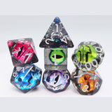A set of translucent polyhedral gaming dice with colorful iridescent and neon patterns, including pink, blue, green, purple, and orange, arranged on a light gray background.