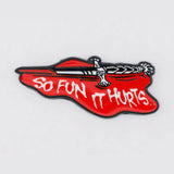 Enamel pin with red background and white text 'So Fun It Hurts' on a gray background